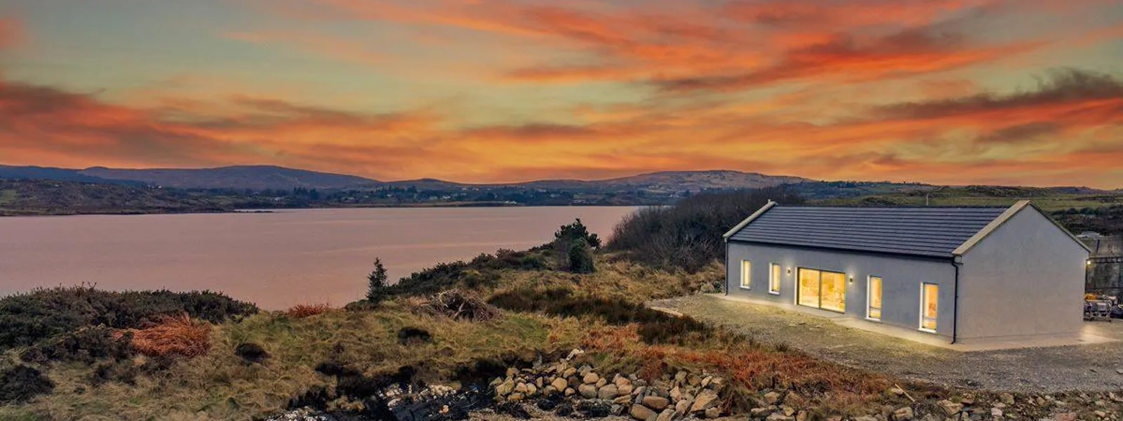 Oyster House with bright lights overlooking Ballinakill Bay at sunset.