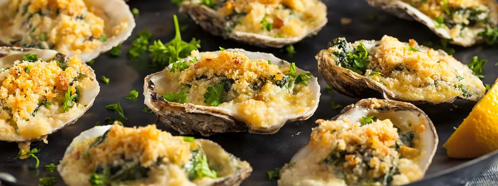 Close-up of cooked oysters on a plate with seasoning and a slice of lemon on the side.