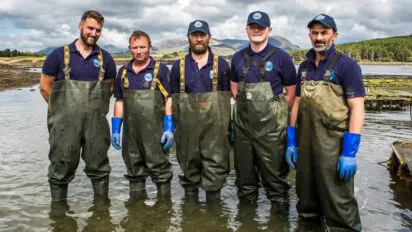 Five DK Connemara Oysters farmers stand together in the water of Ballinakill Bay.