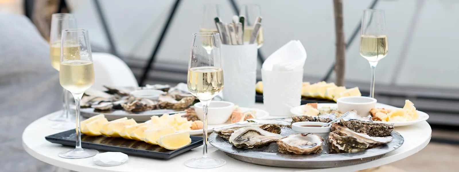 Table with four Oyster platters and sliced lemon platters, glasses of prosecco, knifes and napkins
