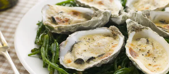 Close-up of a plate of cooked DK Connemara Oysters on a bed of asparagus.